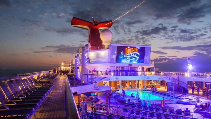 A wide view of Carnival Conquest ship with neon lights on and people enjoying the night life