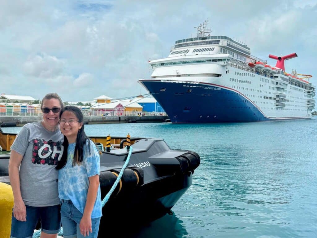 Two women posing a the sea deck with acruise ship at the back